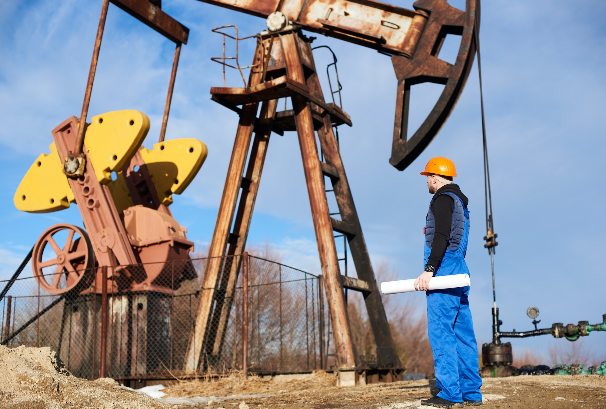 Oil worker standing in the oilfield next to a pump jack with a big paper