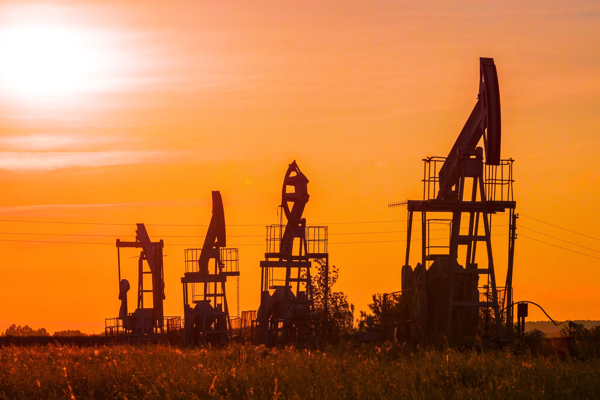The silhouette of oil pumps in a large oil field at sunrise.